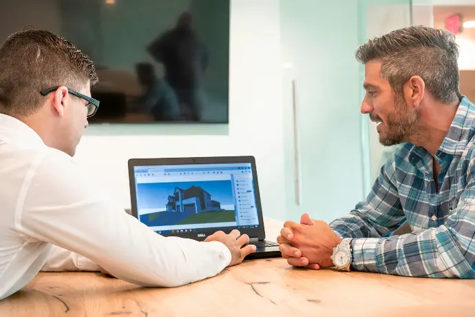 two men sitting at a table with a laptop